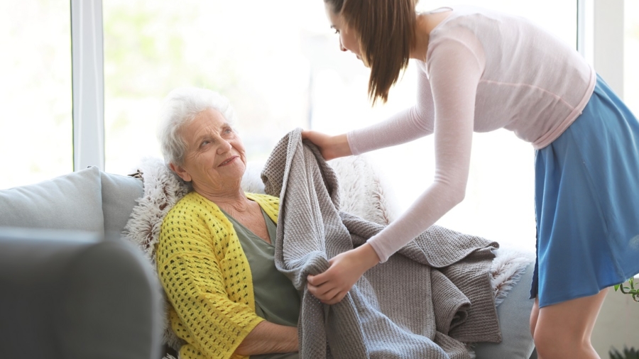 Caregiver covering senior woman with plaid in nursing home