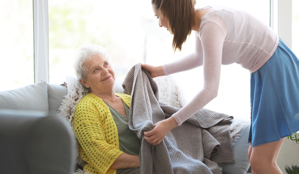 Caregiver covering senior woman with plaid in nursing home